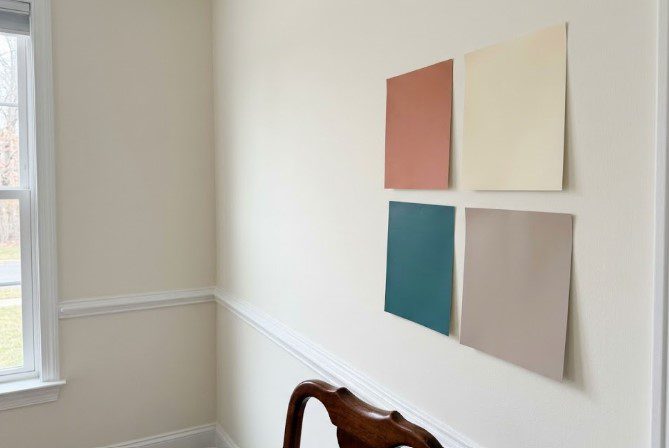 Four large paint color samples taped to a cream dining room wall above the chair rail