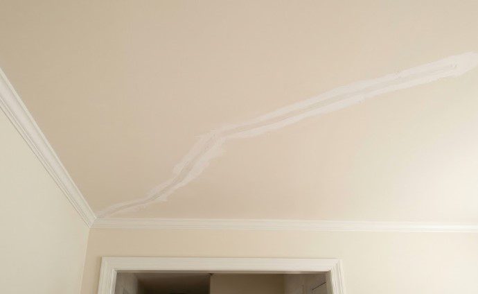 A long crack across a cream-colored ceiling filled and smoothed with white patching compound, near crown molding and a doorway